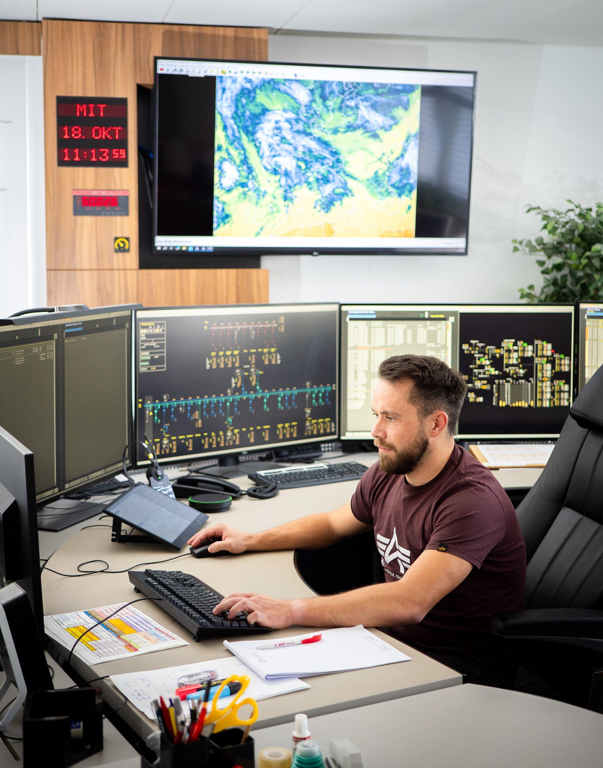 Ein Mitarbeiter sitzt an einem Schreibtisch mit mehreren Computerbildschirmen und überwacht das Stromnetz.