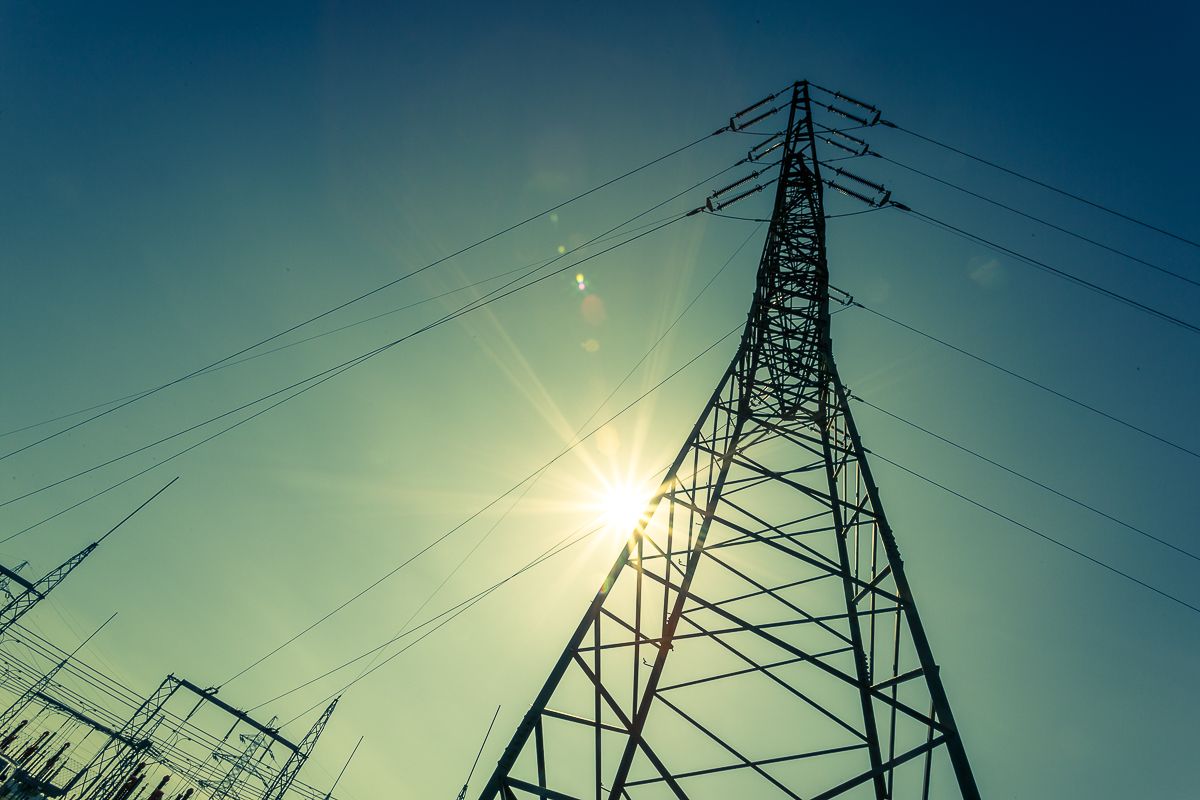 Eine Stromleitung überquert ein Feld mit Windkraftanlagen. Die Leitung ist gespannt und die Windkraftanlagen drehen sich.