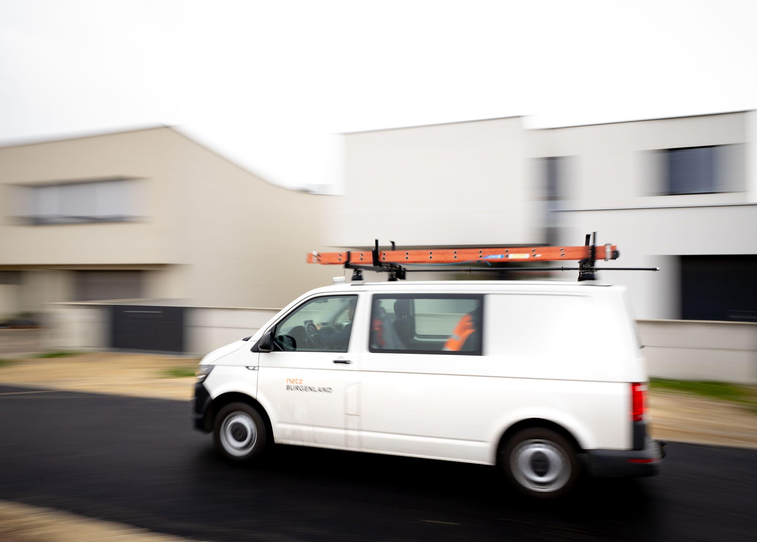 Ein weißer Volkswagen Transporter T5 mit einer Leiter auf dem Dach fährt auf einer Straße im Burgenland. Auf der Seite des Transporters ist das Logo von Netz Burgenland zu sehen.