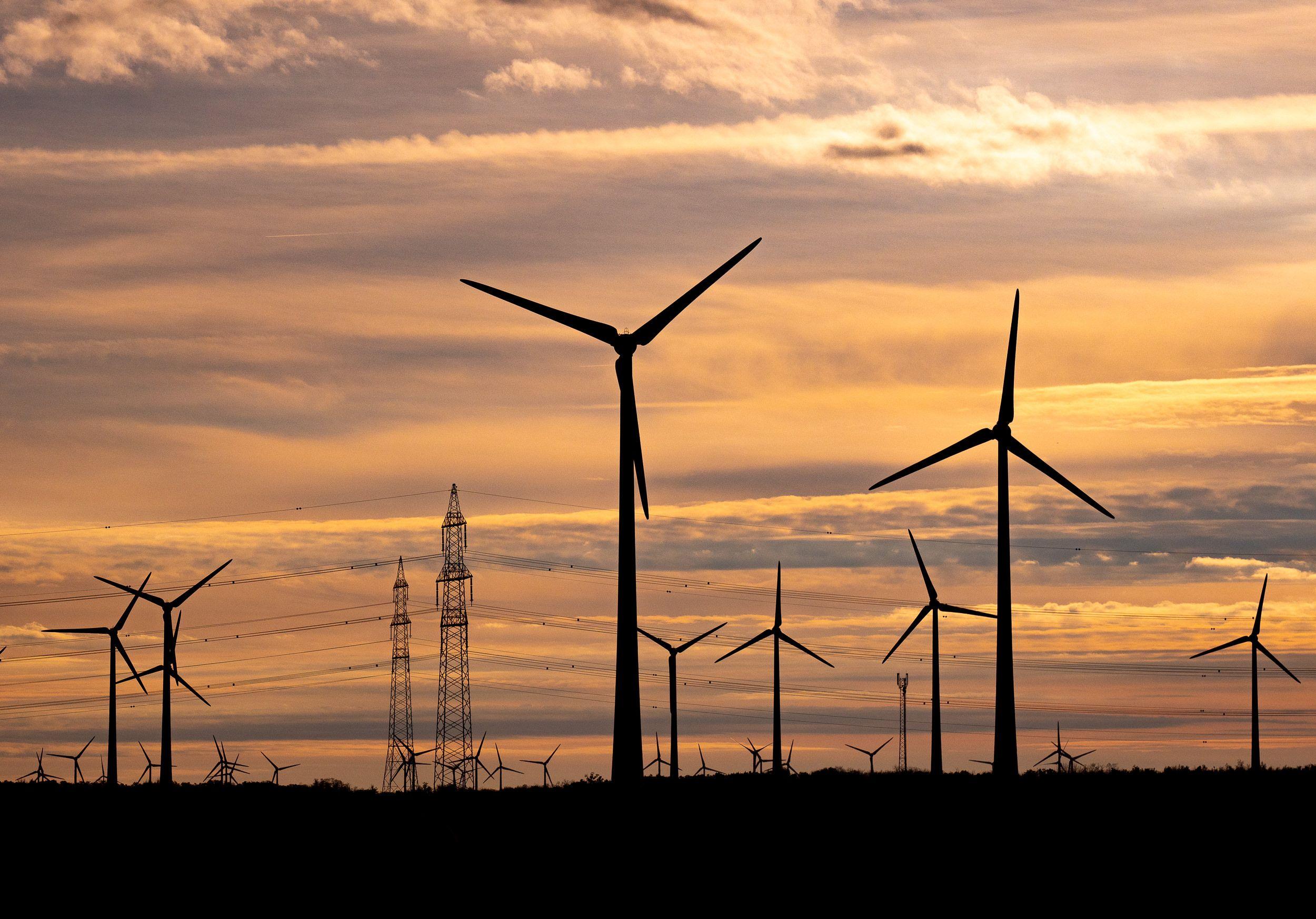 Windräder als Silhouetten gegen einen dramatischen Sonnenuntergangshimmel mit Stromleitungen