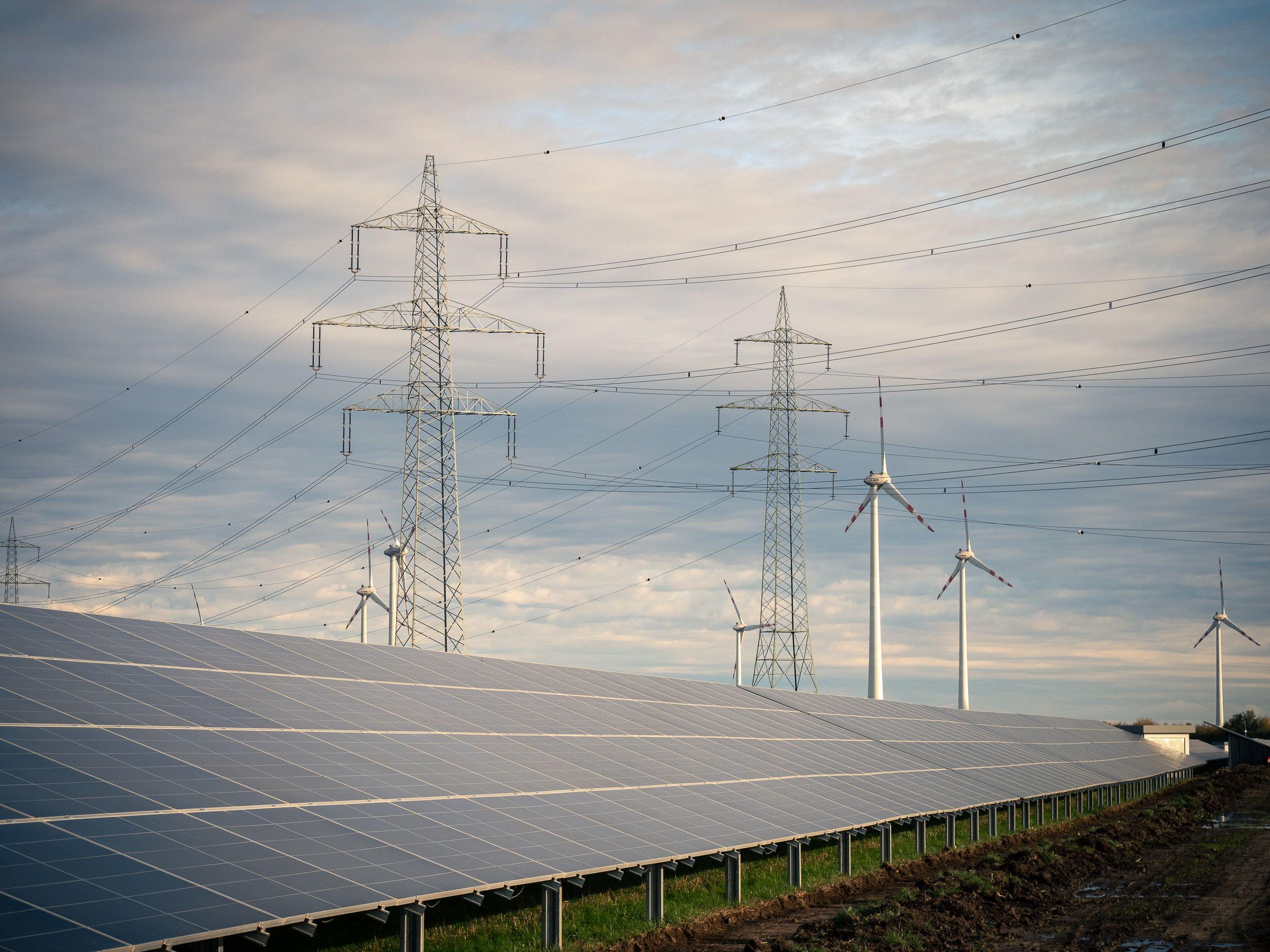 Solarpanele im Vordergrund mit Windkraftanlagen und Strommasten im Hintergrund