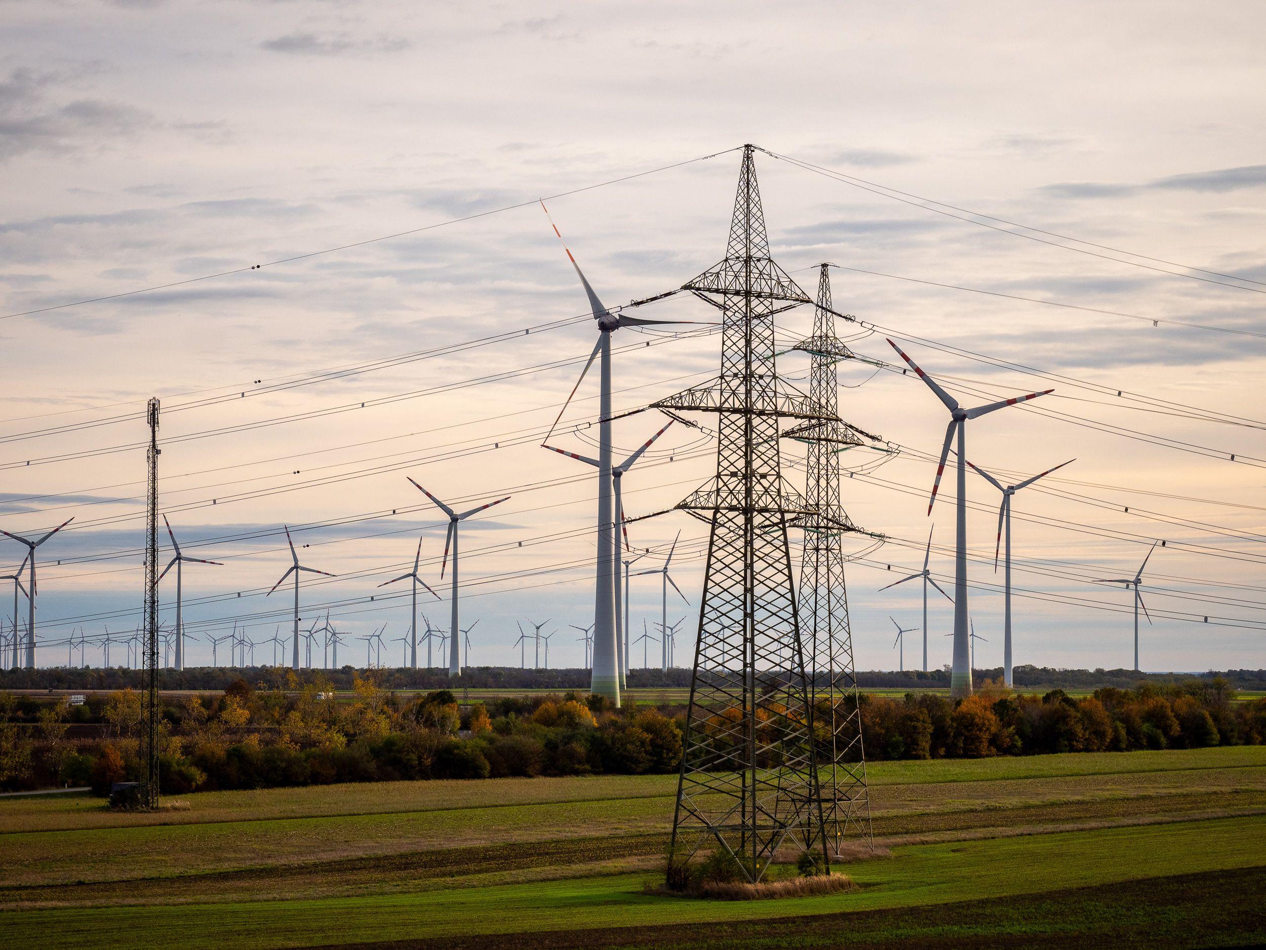 Strommast vor einem Himmel mit Windkraftanlagen im Hintergrund